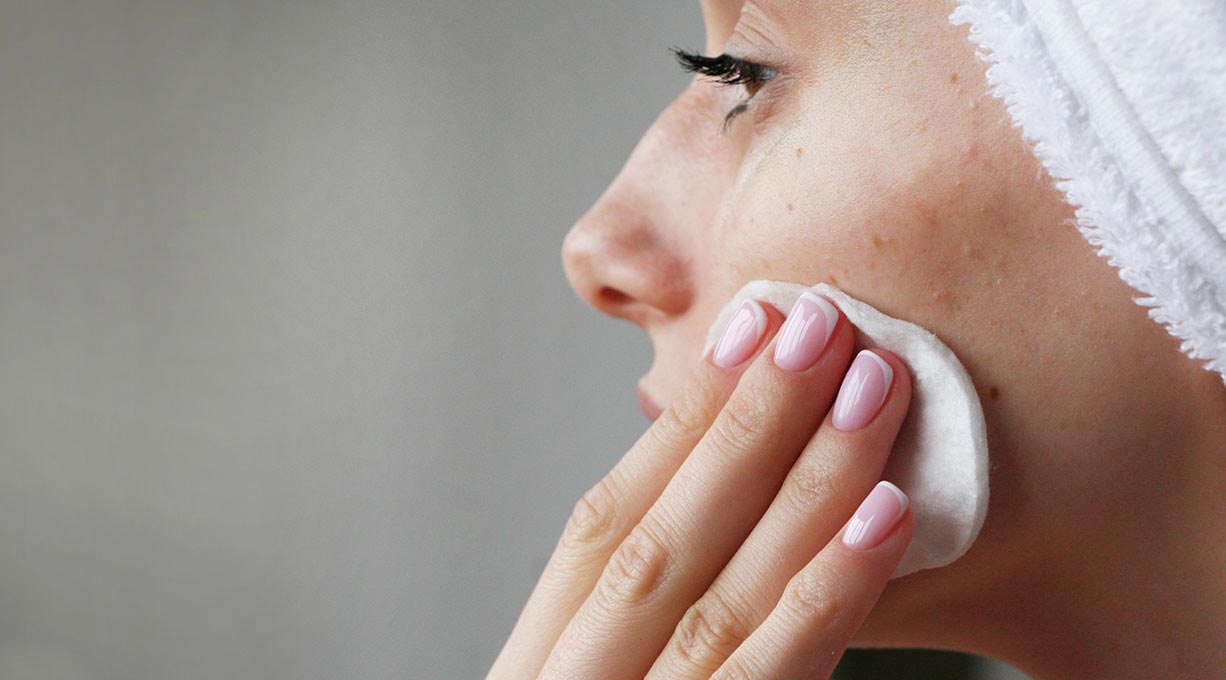Nahaufnahme einer Person die mit einem Wattepad die Wange reinigt Hautpflege gegen Unreinheiten
