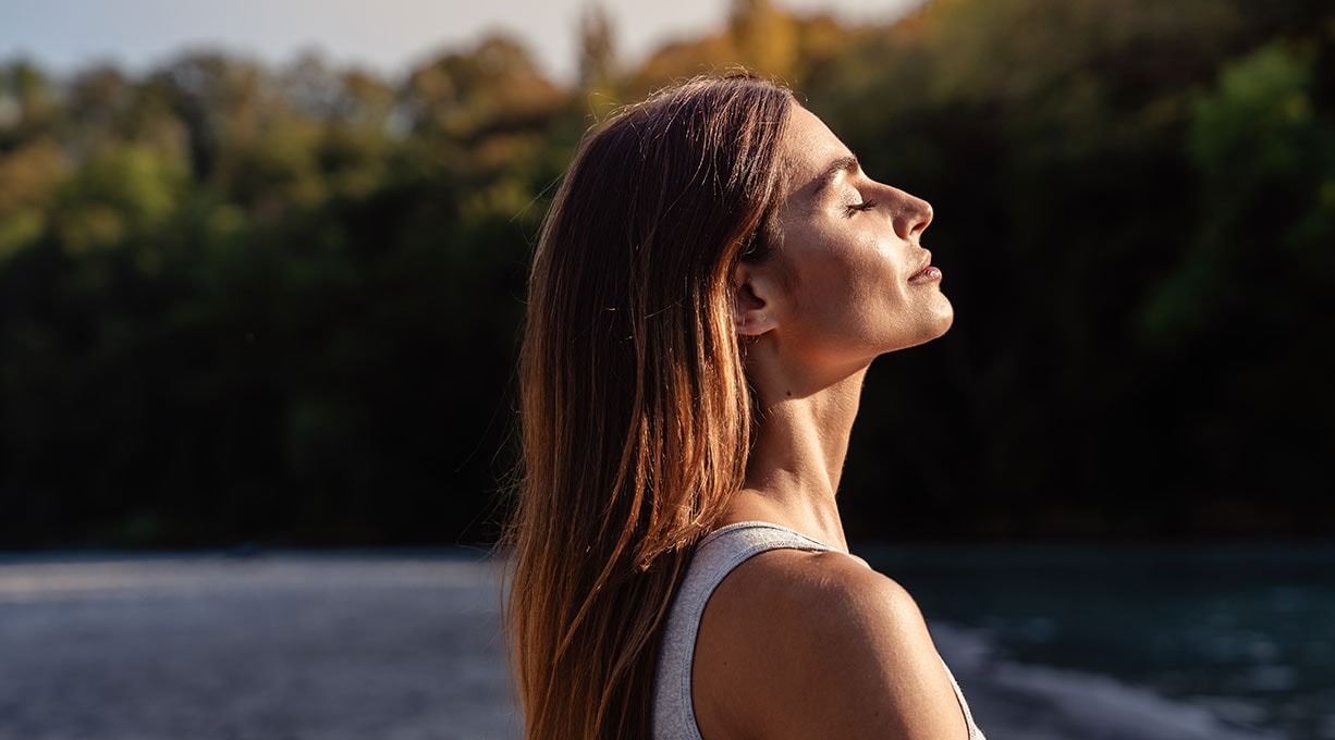 Eine junge Frau steht seitlich in der Sonne mit geschlossenen Augen
