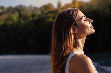 Eine junge Frau steht seitlich in der Sonne mit geschlossenen Augen