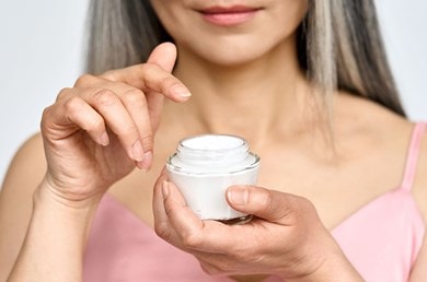 Frau hält offenen Cremetopf gegen Spätakne der Zeigefinger schwebt über der Creme