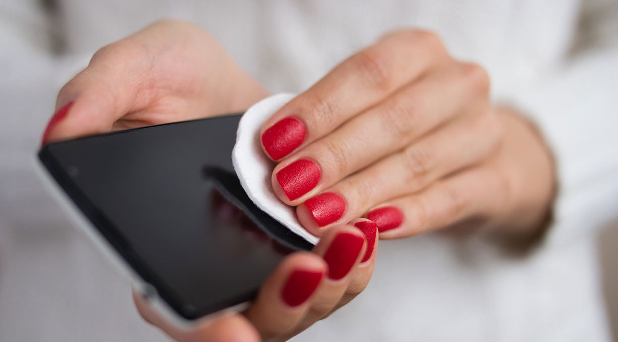 Hände einer Frau reinigen den Handybildschirm mit einem Wattepad