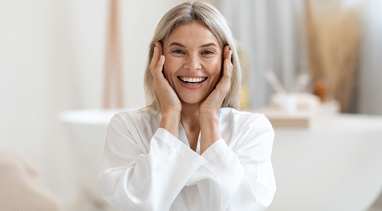 Eine Frau mittleren Alters lächelt und hält ihr Gesicht in den Händen