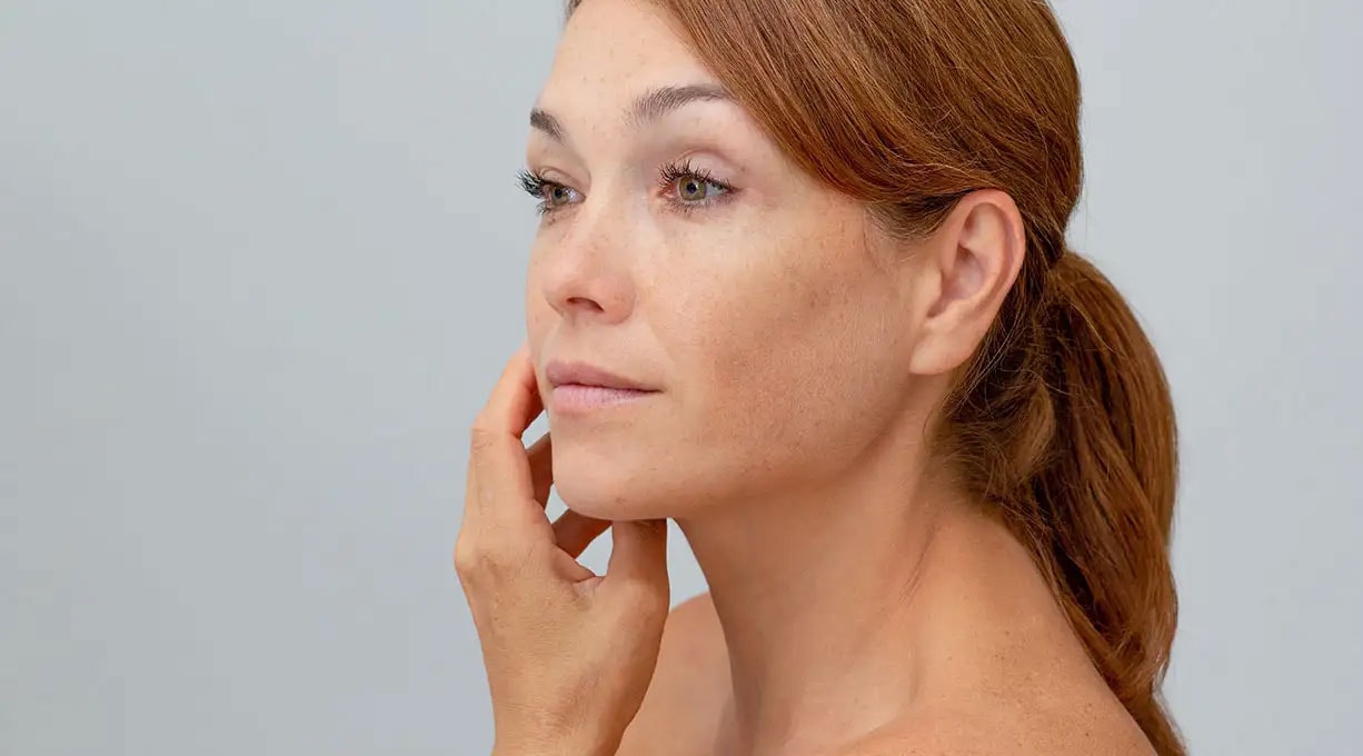 Frau mit roten Haaren und Sommersprossen sieht zur Seite und berührt ihre Wange