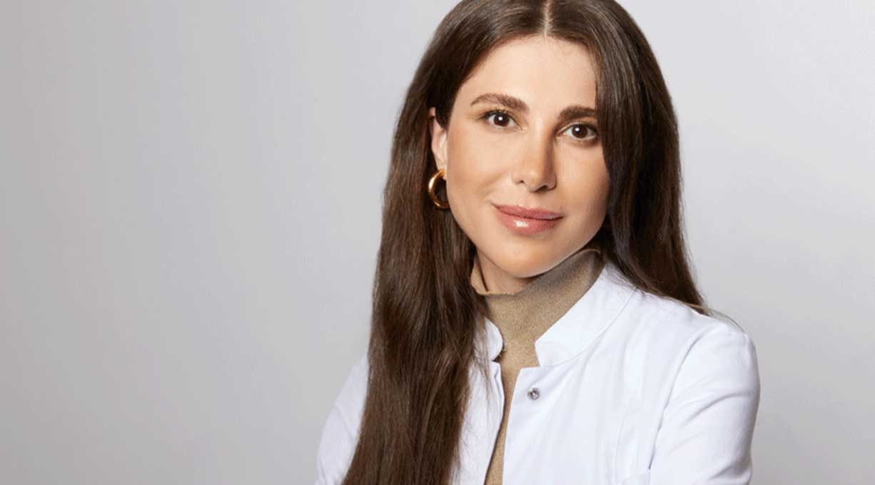 Portrait von Dr. Emi Arpa Dermatologin in weißem Kittel vor neutralem Hintergrund