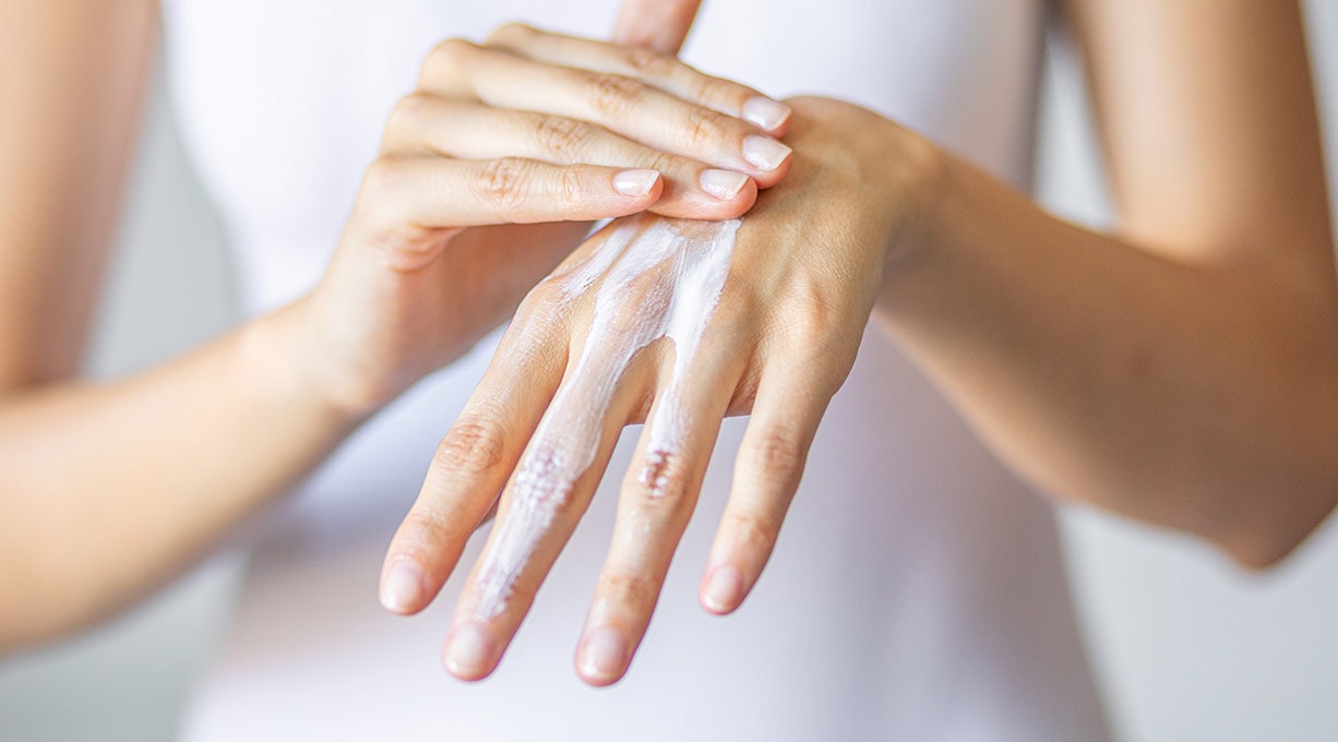 Frau trägt Handcreme auf den Handrücken auf Pflege trockener Haut