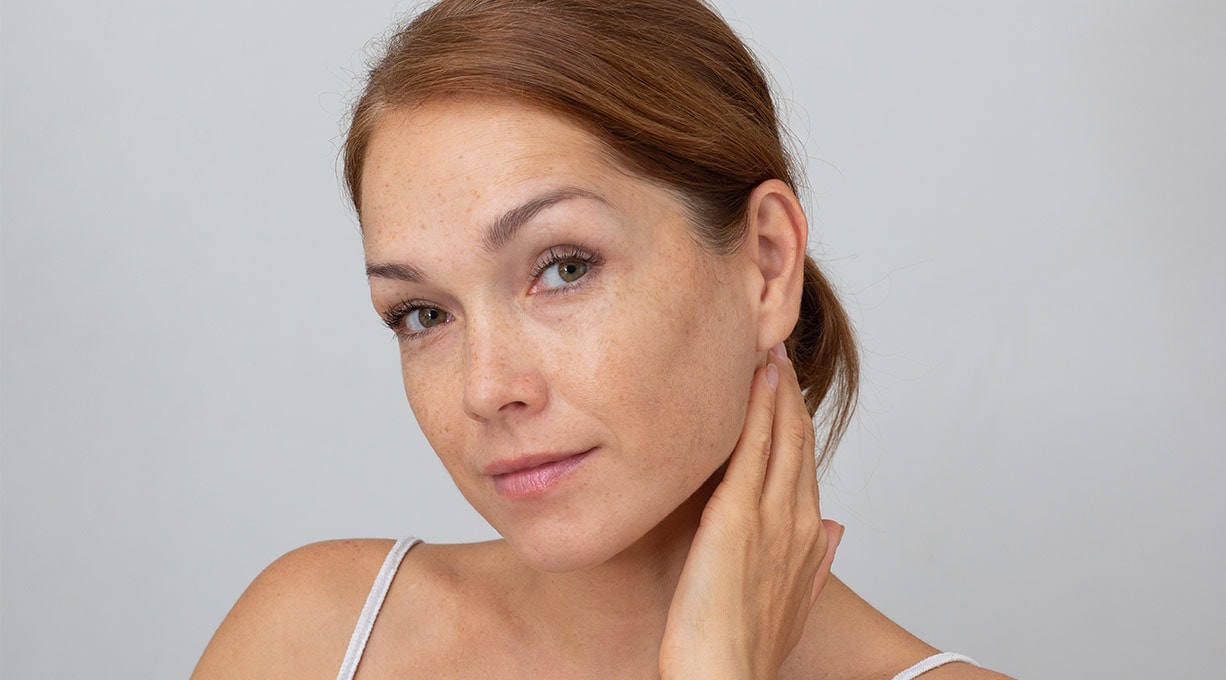 Frau mit Sommersprossen berührt den Kiefer Fokus auf Gesichtshaut und Pflege