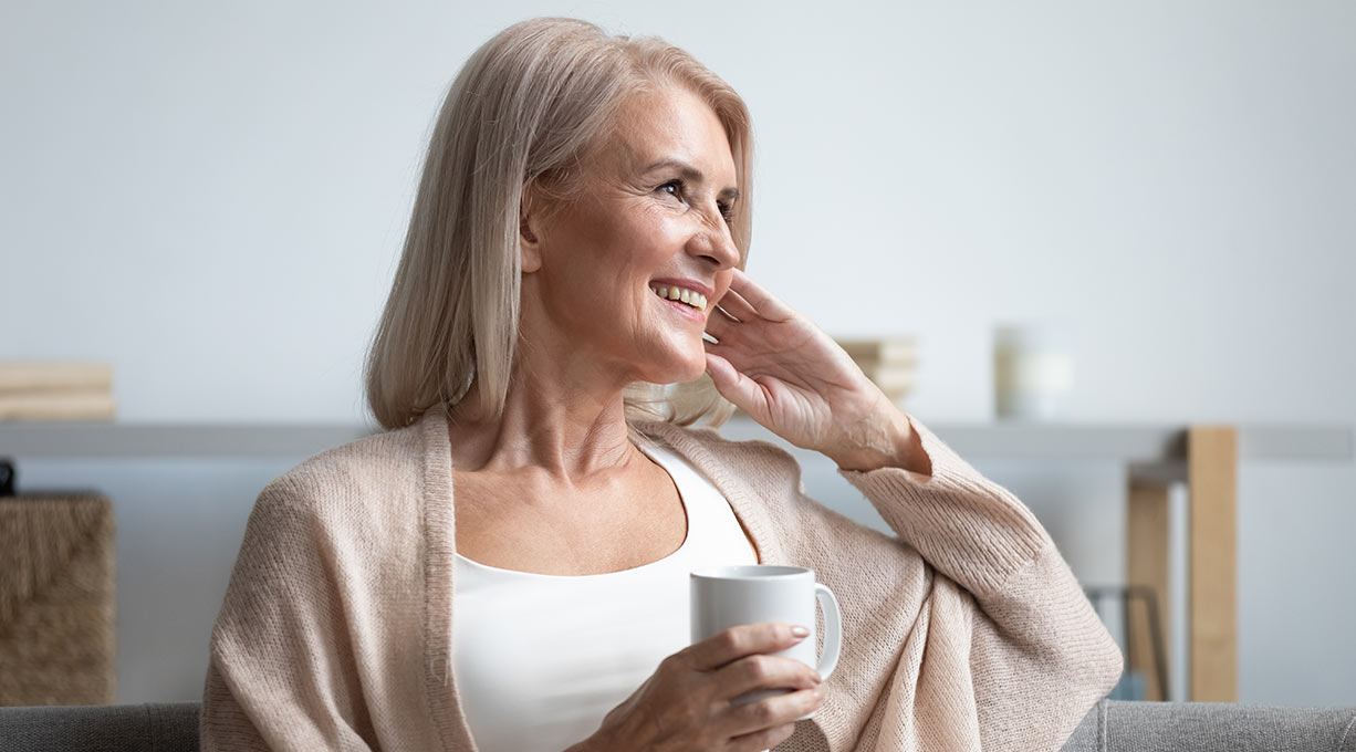 Ältere Frau hält eine Tasse und berührt den Hals blickt zur Seite Fokus auf Wohlbefinden und Hautpflege
