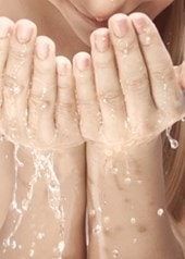 Frau mit langen Haaren wäscht sich das Gesicht mit Wasser