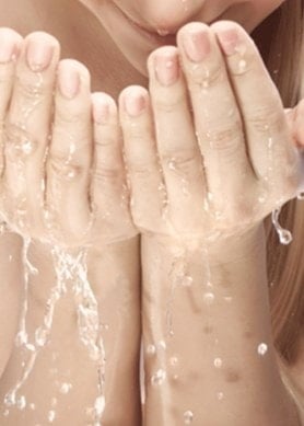 Frau mit langen Haaren wäscht sich das Gesicht mit Wasser