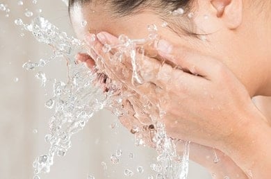 Frau wäscht sich das Gesicht mit klarem Wasser