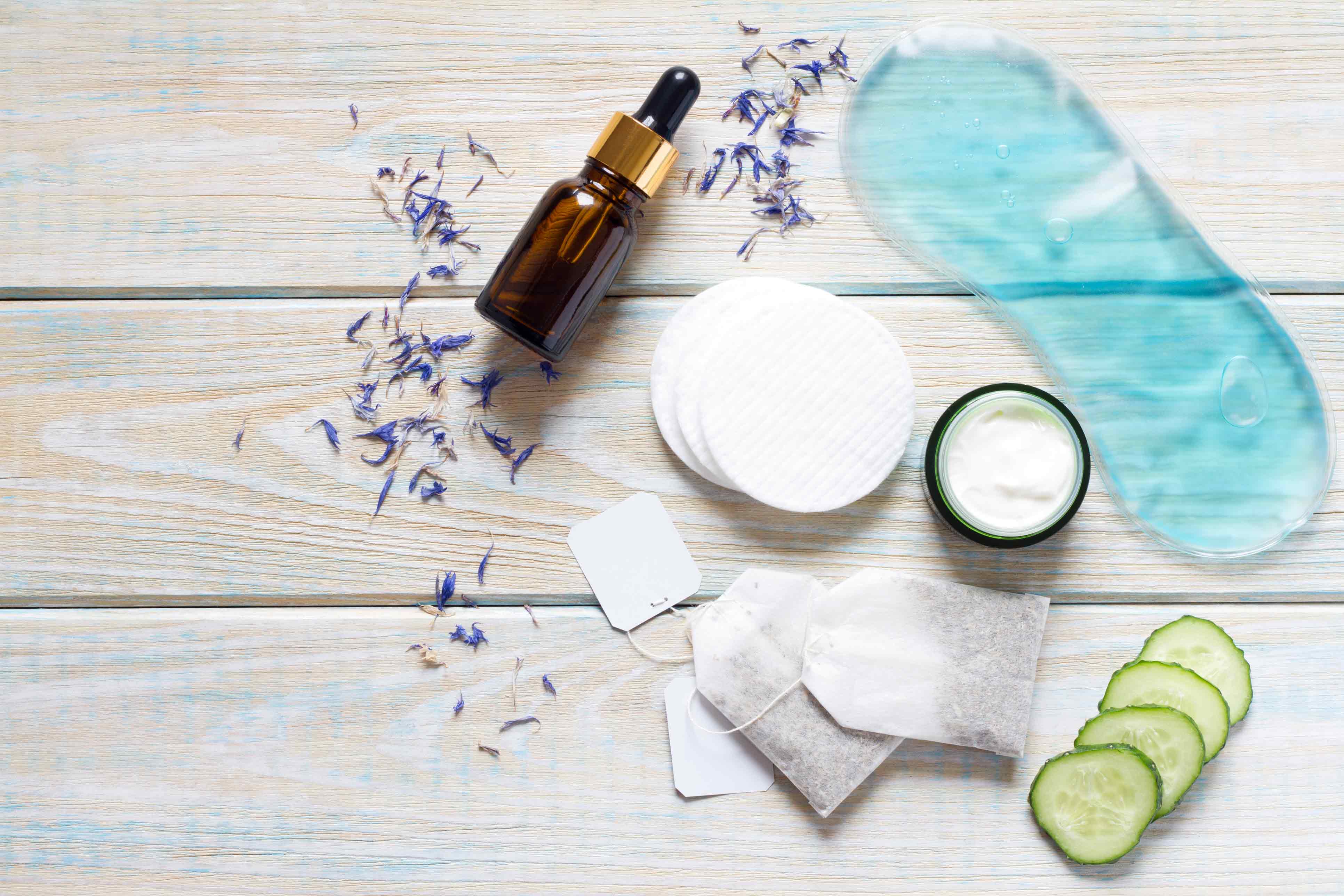 Verschiedene Hautpflegeprodukte wie Creme, Serum, Wattepads, Teebeutel und Gurkenscheiben auf einem Holztisch