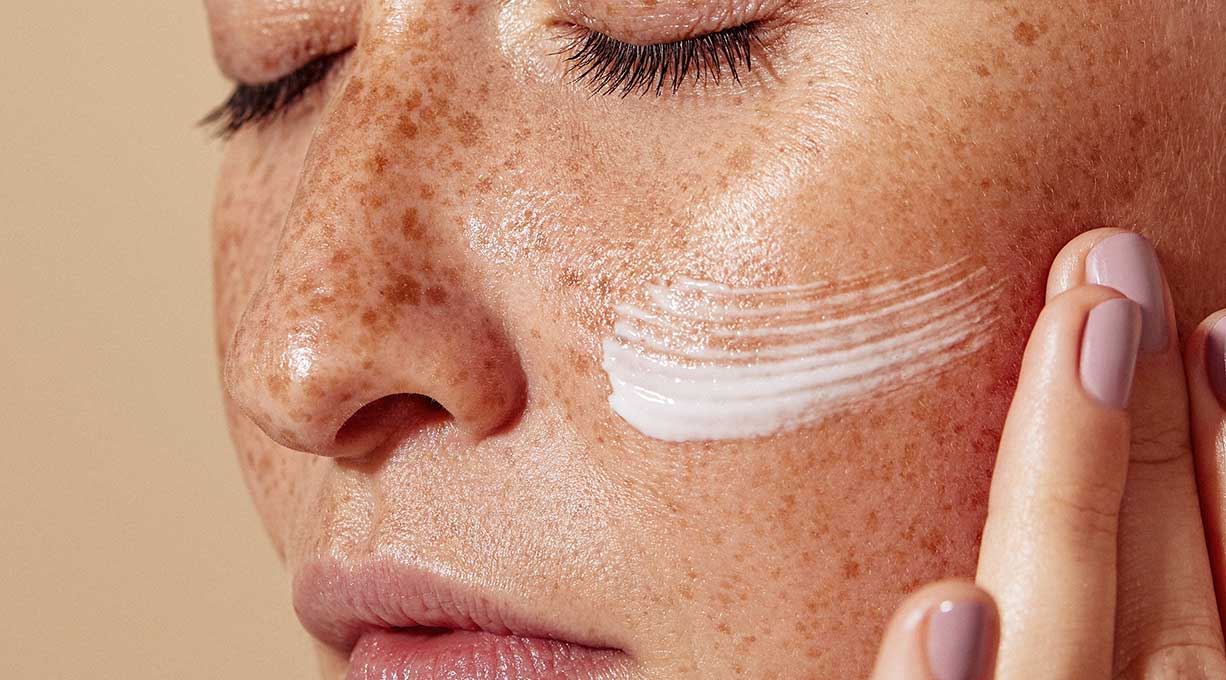 Frau mit Sommersprossen und einem Streifen Gesichtscreme 