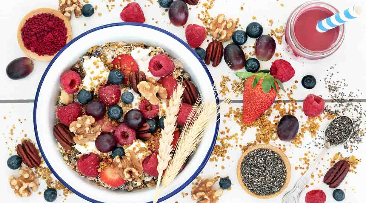 Schale mit Müsli, frischen Beeren, Nüssen und Samen, daneben ein Glas Beerensaft