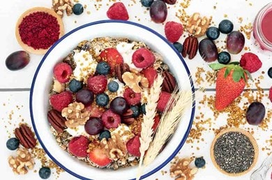 Ein roter Smoothie und ein Porridge mit Erdbeeren, Himbeeren und Heidelbeeren umgeben von Früchten, Nüssen und Chiasamen