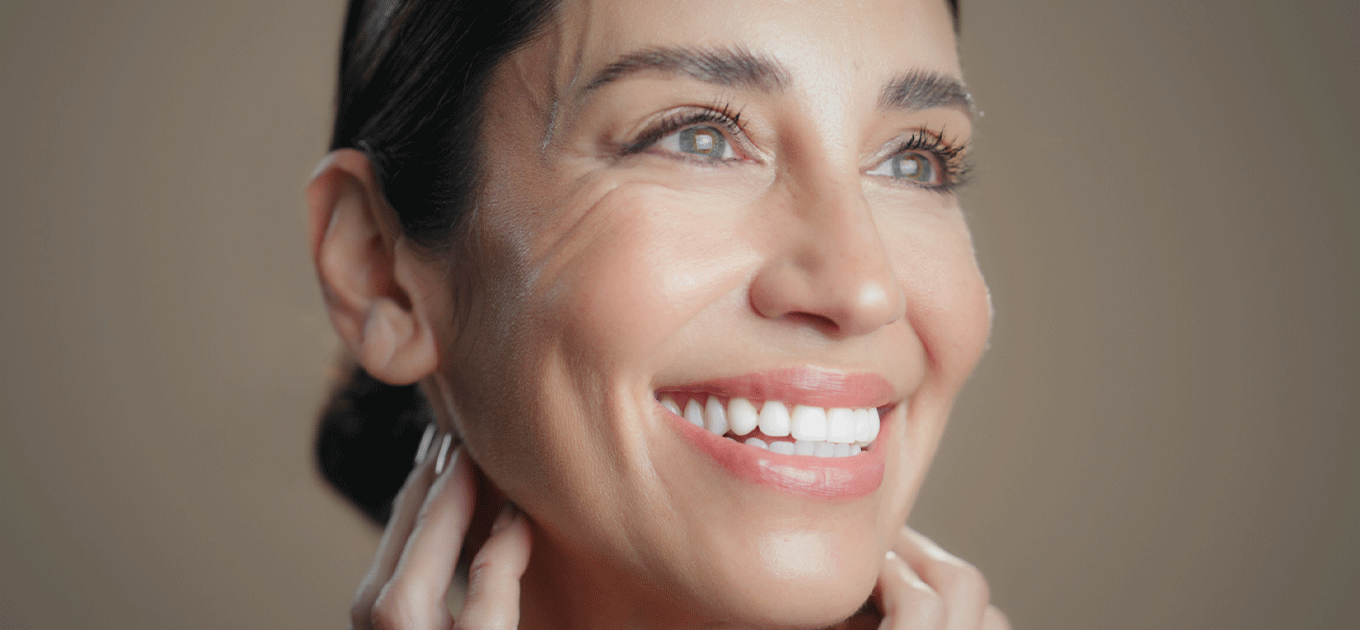 Nahaufnahme einer lächelnden Frau mit glatter Haut, die ihr Gesicht sanft berührt