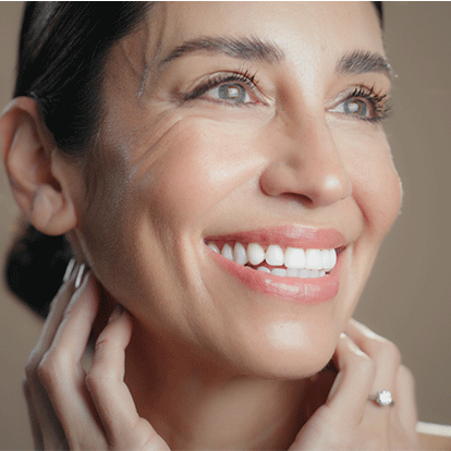 Nahaufnahme einer lächelnden Frau mit glatter Haut, die ihr Gesicht sanft berührt