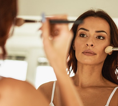 Frau trägt Makeup mit Pinsel vor dem Spiegel auf und schminkt ihre Wangen
