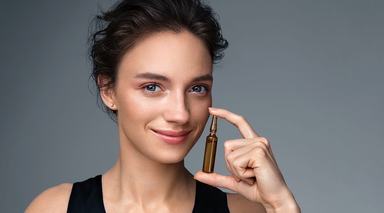 Lächelnde Person hält eine kleine Kollagen Ampulle mit Hautpflegeprodukt zwischen Daumen und Zeigefinger