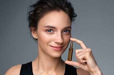 Lächelnde Person hält eine kleine Kollagen Ampulle mit Hautpflegeprodukt zwischen Daumen und Zeigefinger