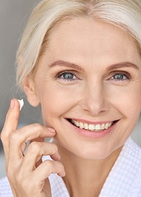 Eine lächelnde Frau hält einen Finger mit Creme nahe an ihre Wange.