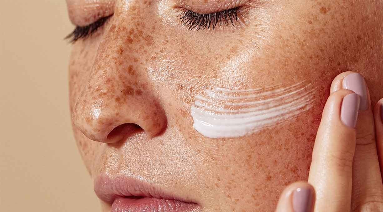 Nahaufnahme eines weiblichen Gesichts mit einem Streifen Creme auf der Wange.