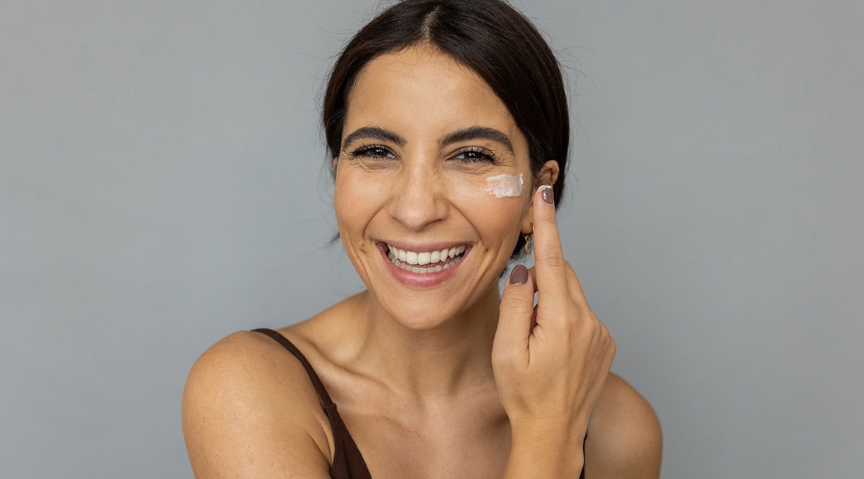 Schauspielerin Chyssanthi Kavazi trägt Gesichtspflege unter dem Auge auf und lächelt in die Kamera