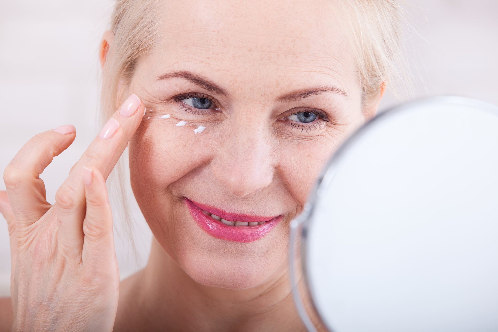 Frau mittleren Alters trägt Augenpflege unter den Augen vor einem Spiegel auf