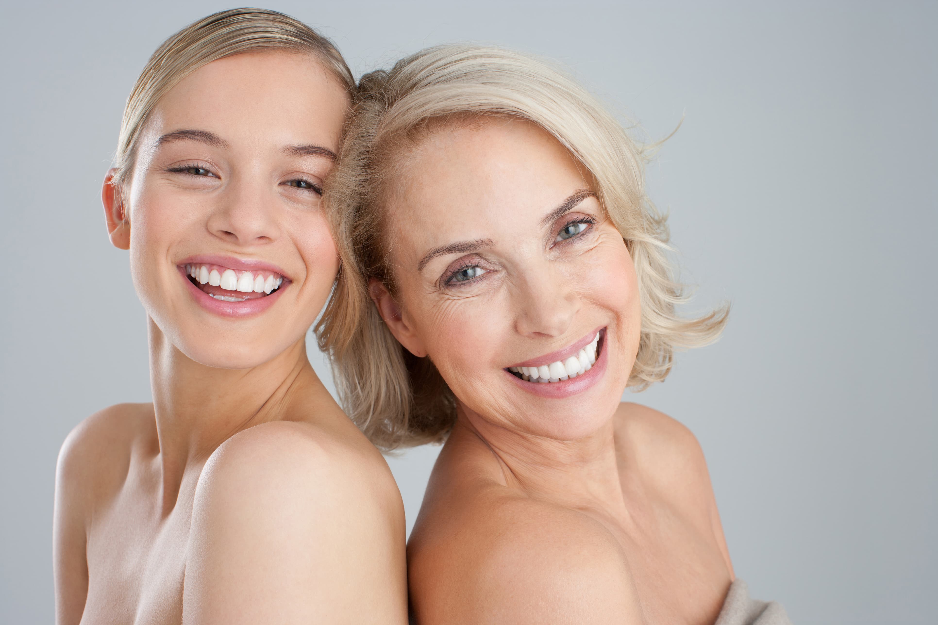 Junge Frau und ältere Frau stehen Schulter an Schulter und lächeln gemeinsam