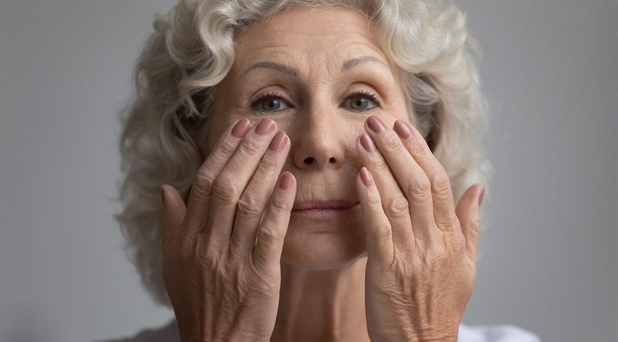 Ältere Frau mit grauen Locken massiert sanft die Haut unter ihren Augen