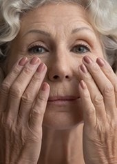 Ältere Frau mit grauen Locken massiert sanft die Haut unter ihren Augen