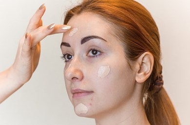 Eine junge Frau bekommt Make-up an manchen Stellen im Gesicht aufgetragen