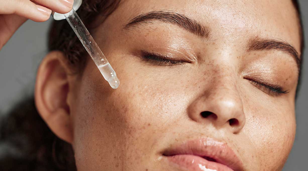 Frau trägt mit Pipette ein Serum auf die Haut im Gesicht auf