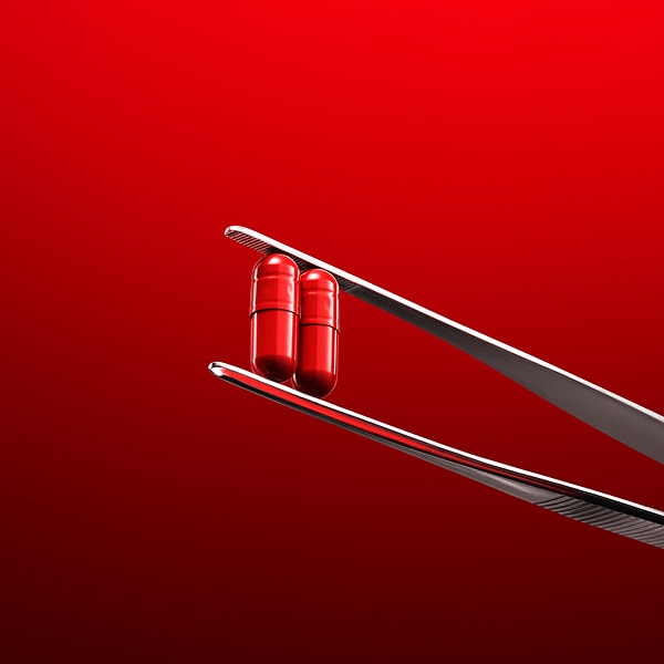 In einer Pinzette werden zwei Kapseln als Symbol für eine Nahrungsergänzung mit Kollagen gehalten