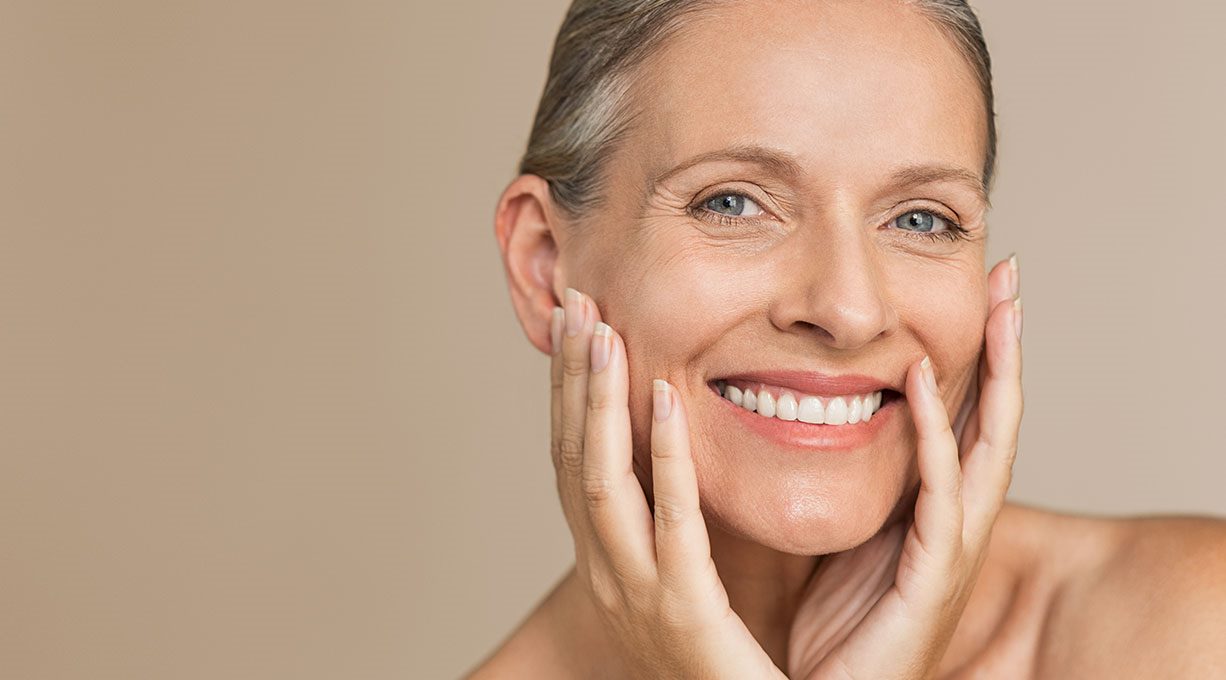 Eine Frau mit strahlendem Lächeln berührt ihre Wangen mit beiden Händen.