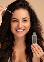 Frau mit langen Haaren appliziert Gesichtsserum mit Pipette und lächelt