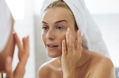 Frau trägt Anti-Aging-Creme unter dem Auge auf, Fokus auf Faltenpflege.