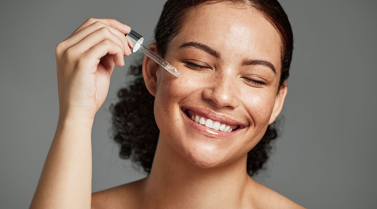 Frau trägt leichtes Serum auf die Wange auf, Pflege für fettige Haut.