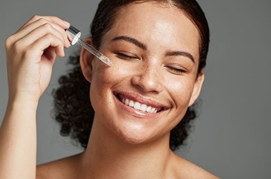 Frau trägt leichtes Serum auf die Wange auf, Pflege für fettige Haut.