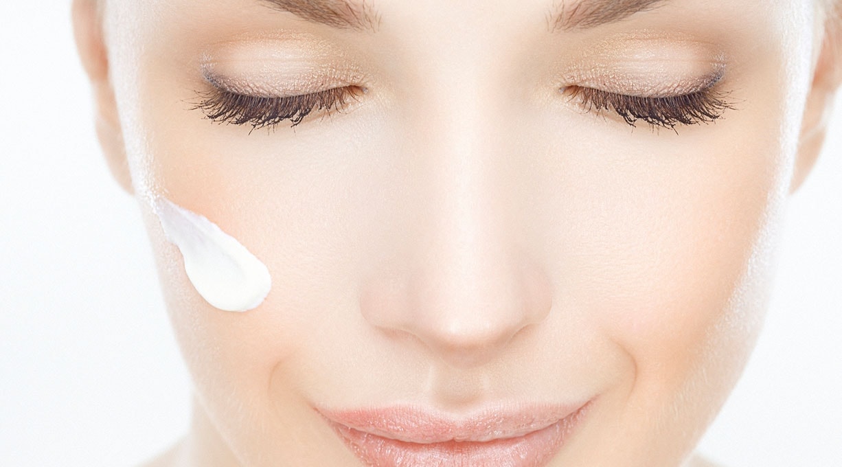 Gesicht einer jungen Frau mit einem Klecks weißer Creme auf einer Wange