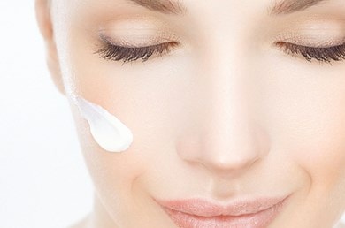 Gesicht einer jungen Frau mit einem Klecks weißer Creme auf einer Wange