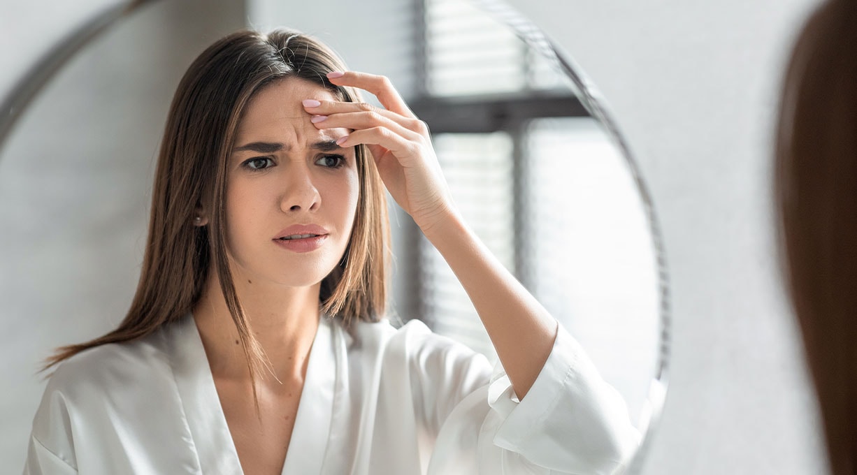 Frau vor dem Spiegel mit Zornesfalte fasst sich an die Stirn