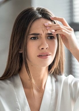 Frau vor dem Spiegel mit Zornesfalte fasst sich an die Stirn