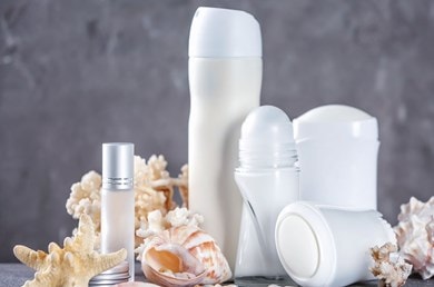 Verschiedene Arten von Deos wie Deo-Spray und Deo-Stick mit Muscheln als Deko im Hintergrund