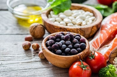 Verschiedene Schalen auf einem Holztisch mit Früchten, Nüssen, Fisch und Gemüse wie Tomaten und Brokkoli