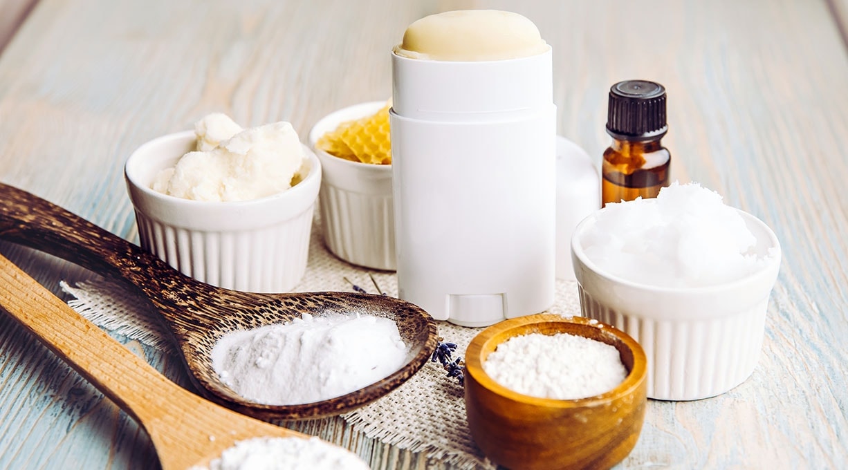 Deo-Stick und natürliche Inhaltsstoffe wie Sheabutter und Natron auf Holztisch.