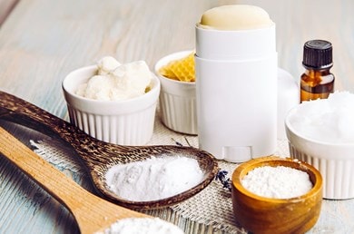 Deo-Stick und natürliche Inhaltsstoffe wie Sheabutter und Natron auf Holztisch.