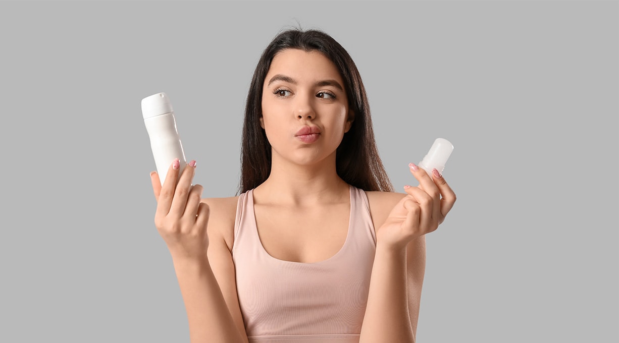 Frau vergleicht Spray und Deo-Stick, um das passende Produkt gegen Schwitzen zu wählen.