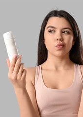 Frau vergleicht Spray und Deo-Stick, um das passende Produkt gegen Schwitzen zu wählen.