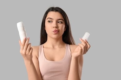 Frau vergleicht Spray und Deo-Stick, um das passende Produkt gegen Schwitzen zu wählen.