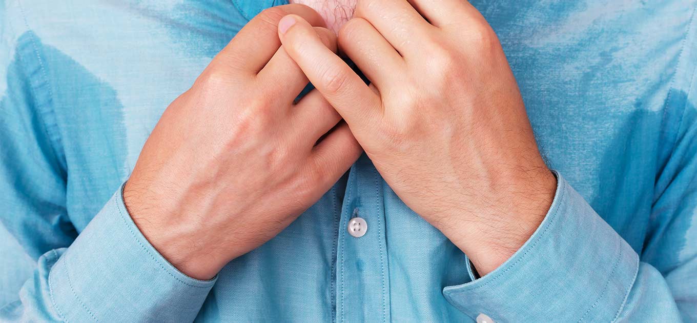 Mann mit schweißnassem Hemd im Brustbereich hält den Kragen mit beiden Händen fest